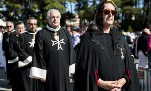 Uczestnicy procesji w czarnych szatach z białym krzyżem maltańskim. Kobieta w okularach i czarnej woalce.