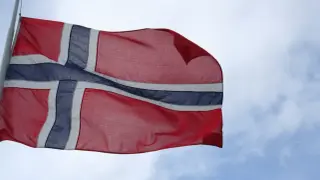 Flaga Norwegii powiewa na wietrze na tle błękitnego nieba z chmurami.