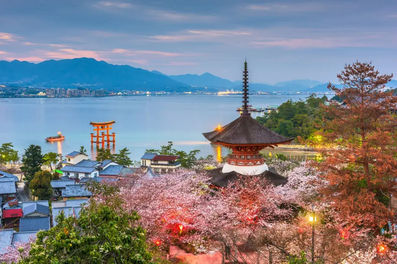Wiosna na wyspach Japonii: kwitnące wiśnie otaczają pagodę i bramę torii na tle spokojnej wody i gór.