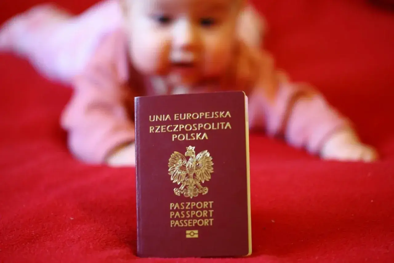 Dziecko w tle, przed nim polski paszport. Czas na złożenie wniosku o paszport dla malucha.